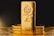 A stack of gold bars is prominently displayed. The forefront features a larger gold bar with intricate engravings, including a lion emblem and inscriptions indicating its weight as one kilo of fine gold. The scene is set against a dark background with a warm, golden glow, highlighting the richness and value of the bars.