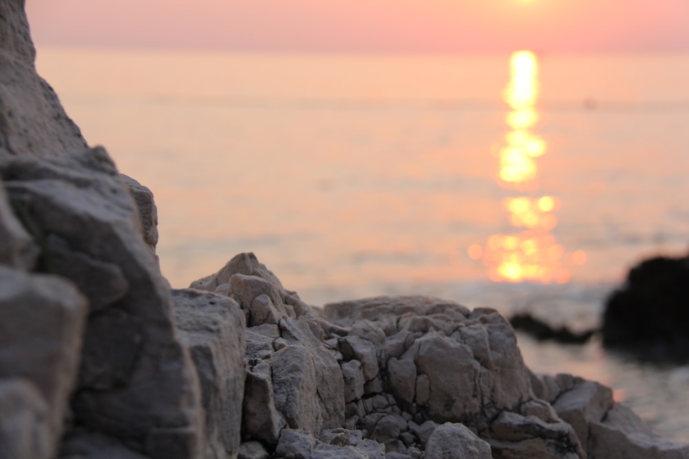 the sun is setting over the water and rocks