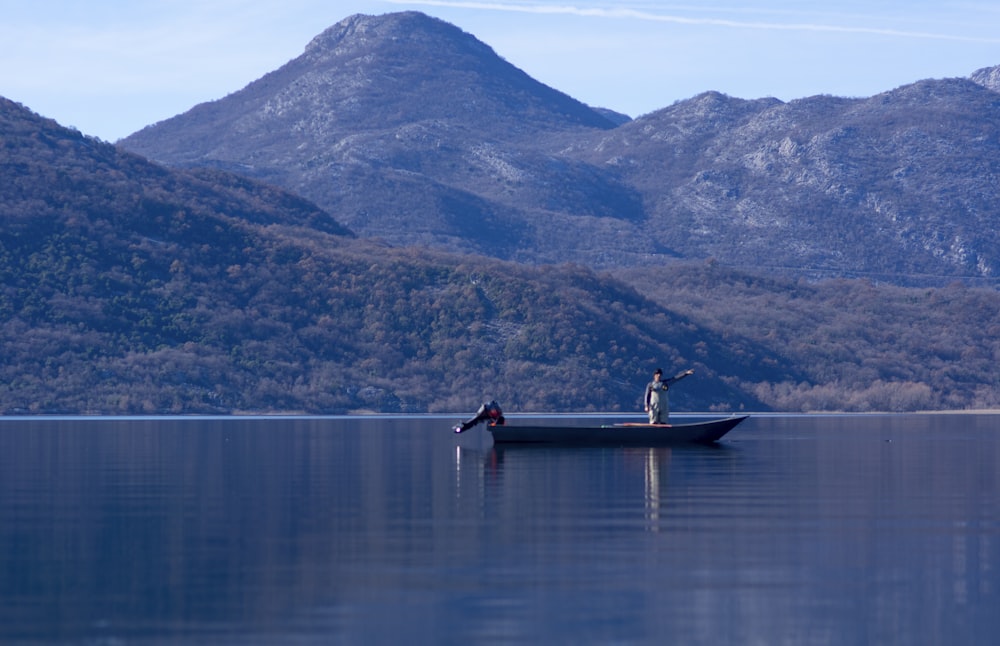 a man in a boat on a lake with mountains in the background