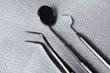 A set of dental instruments is arranged on a fabric with a hexagonal pattern. The tools include a dental mirror, a scaler, forceps, and a pair of tweezers, which are all made of shiny metal.