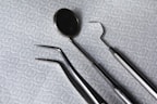 A set of dental instruments is arranged on a fabric with a hexagonal pattern. The tools include a dental mirror, a scaler, forceps, and a pair of tweezers, which are all made of shiny metal.