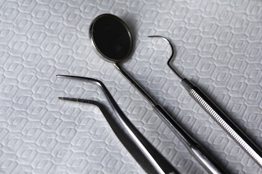 A set of dental instruments is arranged on a fabric with a hexagonal pattern. The tools include a dental mirror, a scaler, forceps, and a pair of tweezers, which are all made of shiny metal.