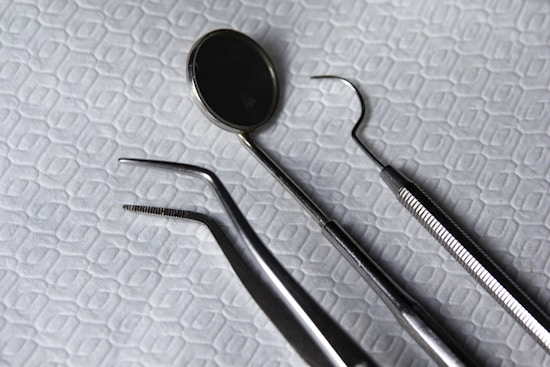 A set of dental instruments is arranged on a fabric with a hexagonal pattern. The tools include a dental mirror, a scaler, forceps, and a pair of tweezers, which are all made of shiny metal.