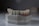 A dental mold featuring a set of artificial teeth is placed on a smooth surface. The mold is crafted from a greyish material with slight discolorations and scribbles. The artificial teeth are aligned neatly, resembling a realistic dental setup with gums depicted in a darker, reddish shade.