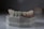 A dental mold featuring a set of artificial teeth is placed on a smooth surface. The mold is crafted from a greyish material with slight discolorations and scribbles. The artificial teeth are aligned neatly, resembling a realistic dental setup with gums depicted in a darker, reddish shade.
