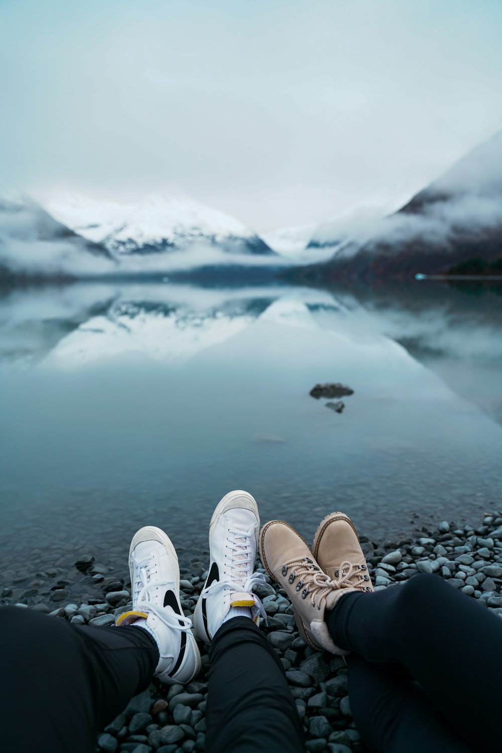 two people sitting on a rocky shore with a lake in the background