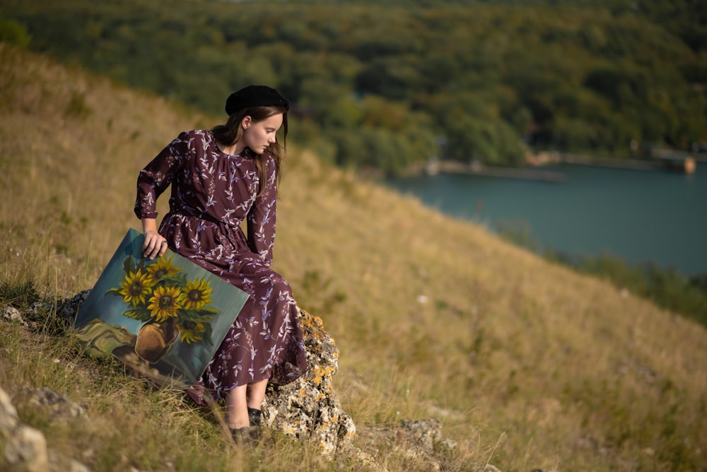 a woman sitting on a hill holding a pillow with a picture of a sunflower