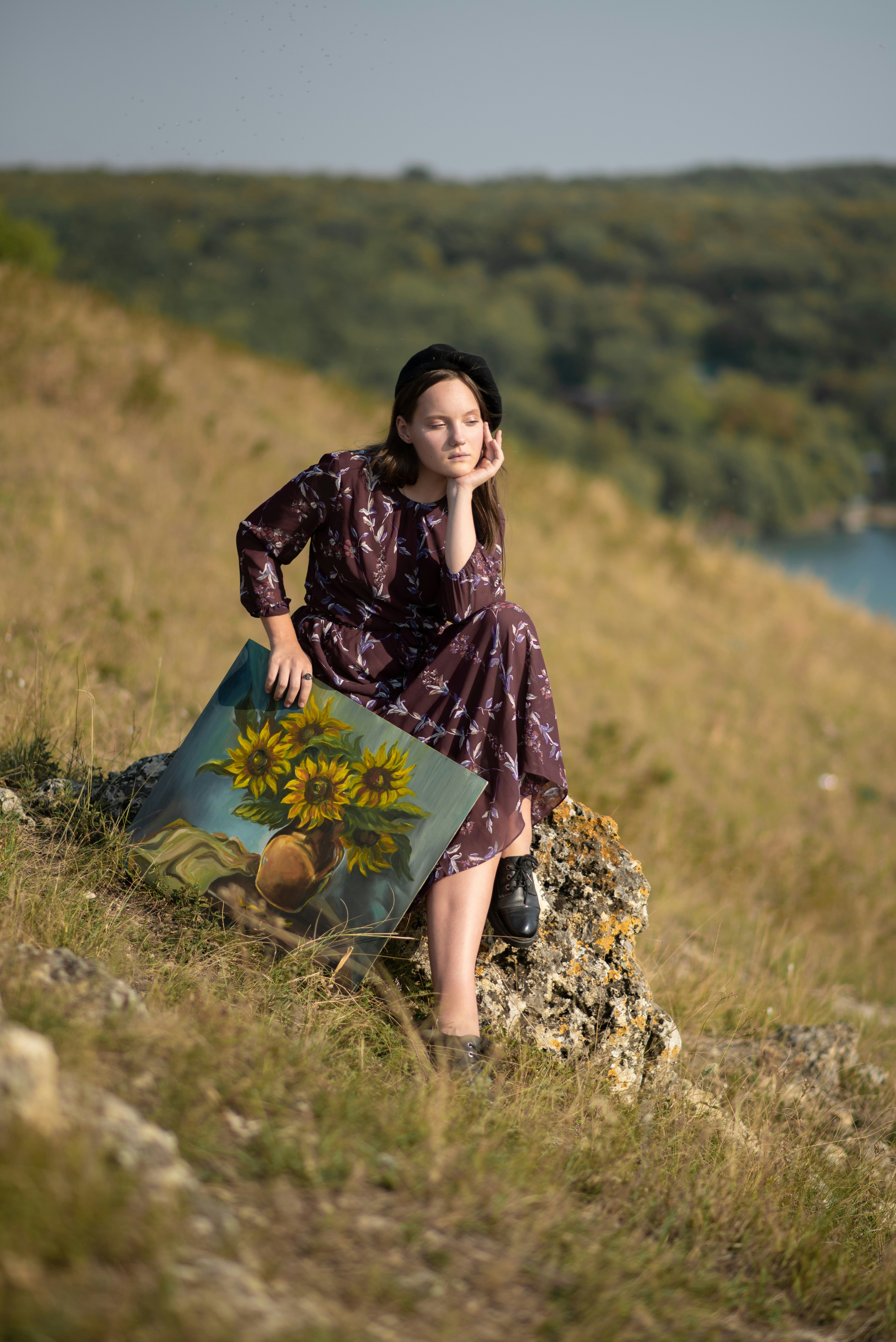 a woman sitting on a rock with a painting of a sunflower