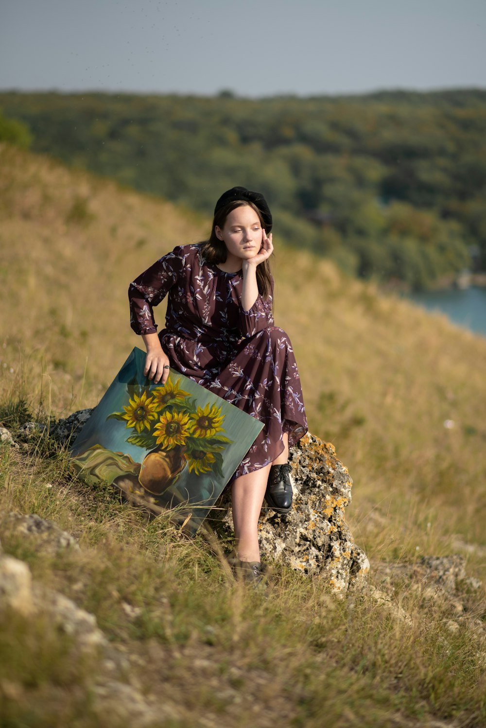 a woman sitting on a rock with a painting of a sunflower