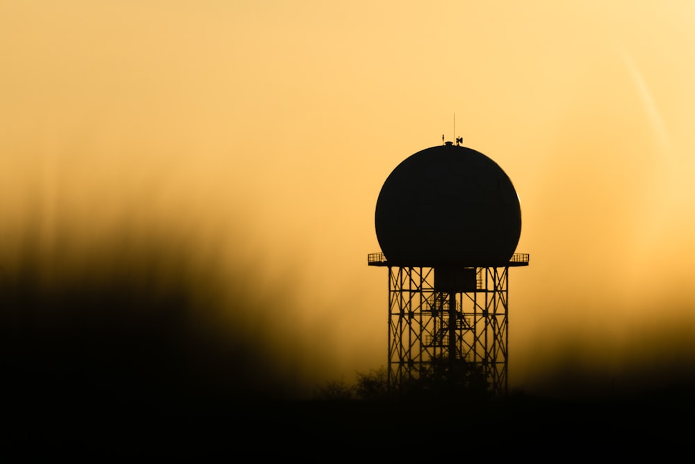 a silhouette of a water tower against a yellow sky