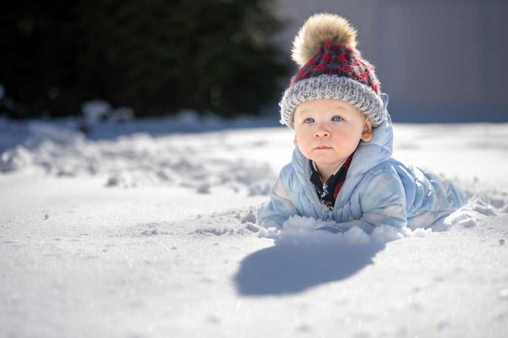 a small child laying in the snow wearing a hat