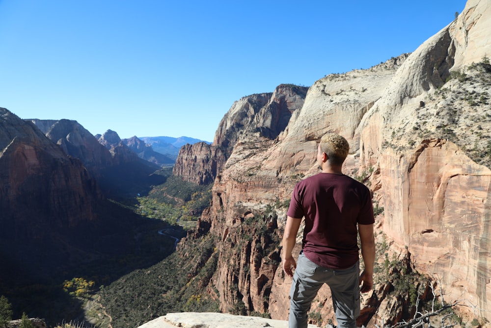 um homem de pé no topo de um penhasco com vista para um vale