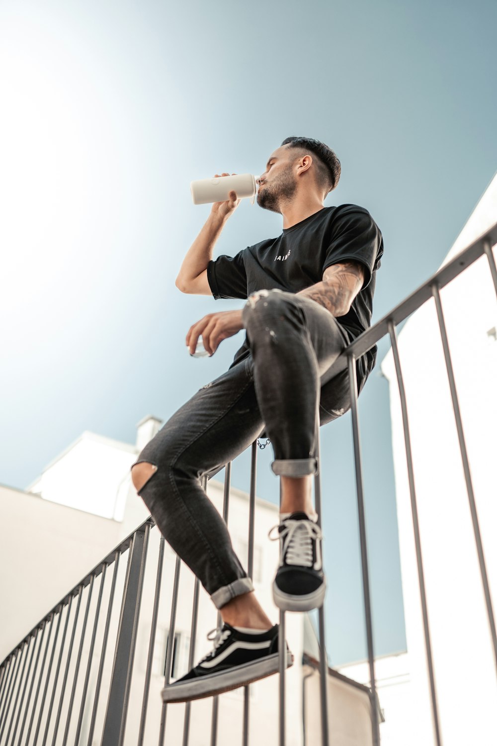 a man sitting on a railing drinking from a bottle