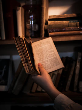 A robot hand holding a vintage book under soft lighting.