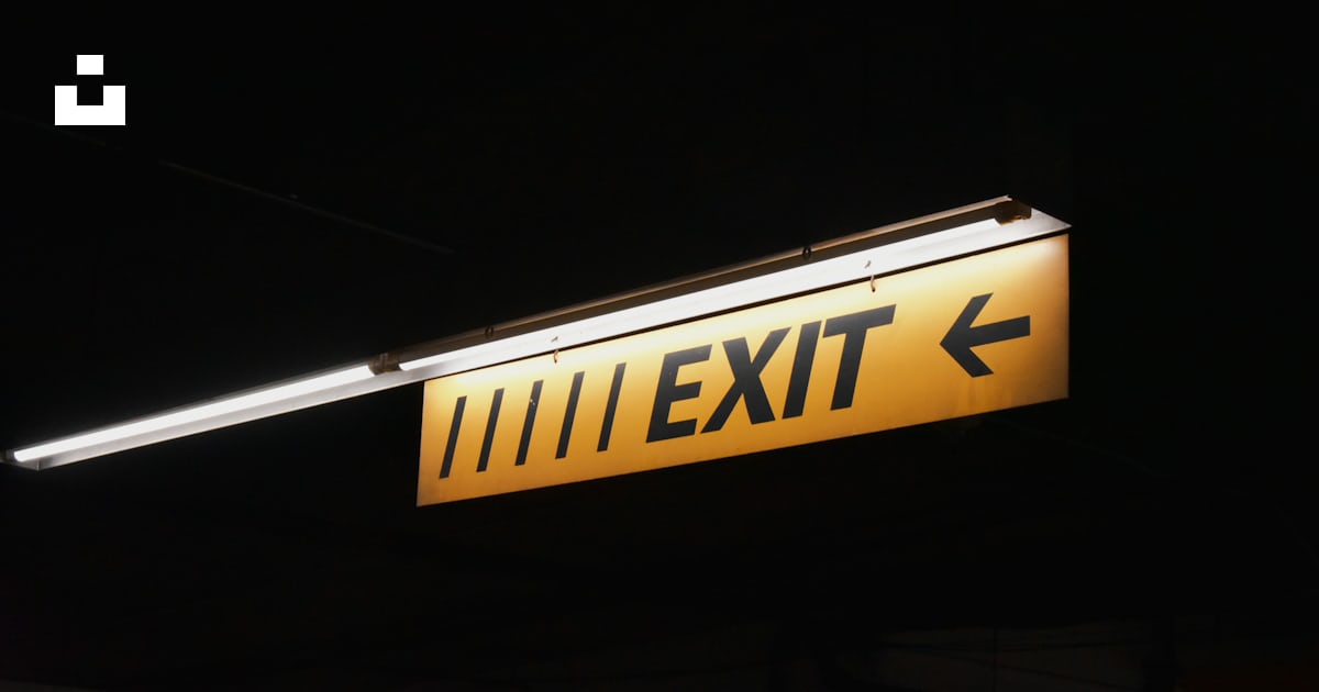 A yellow exit sign hanging from the side of a building photo – Free ...