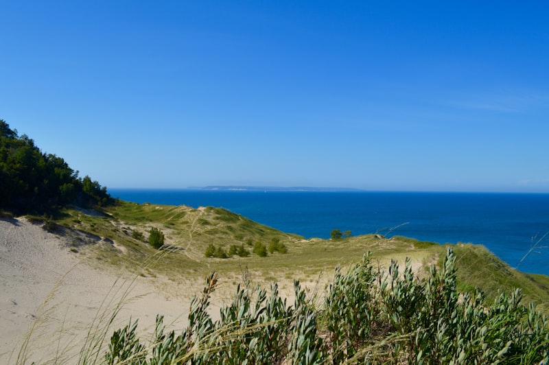 Grassy sand dunes dropping toward the deep blue water of Lake Michigan under a clear sky