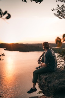 a man sitting on top of a rock next to a body of water