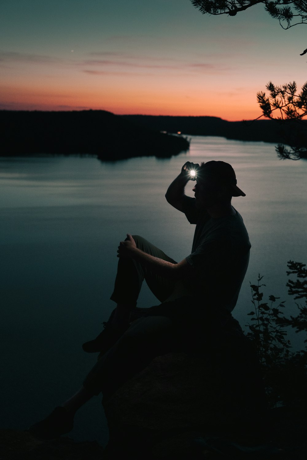 a man sitting on top of a rock next to a body of water