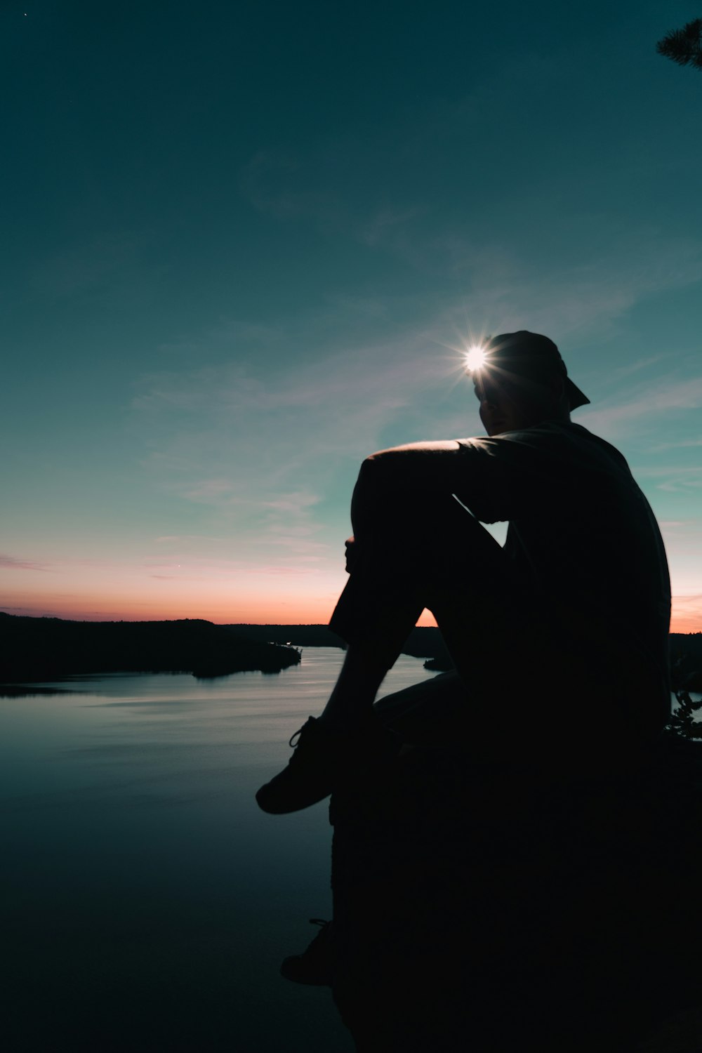 夕暮れ時に湖のほとりに座っている男