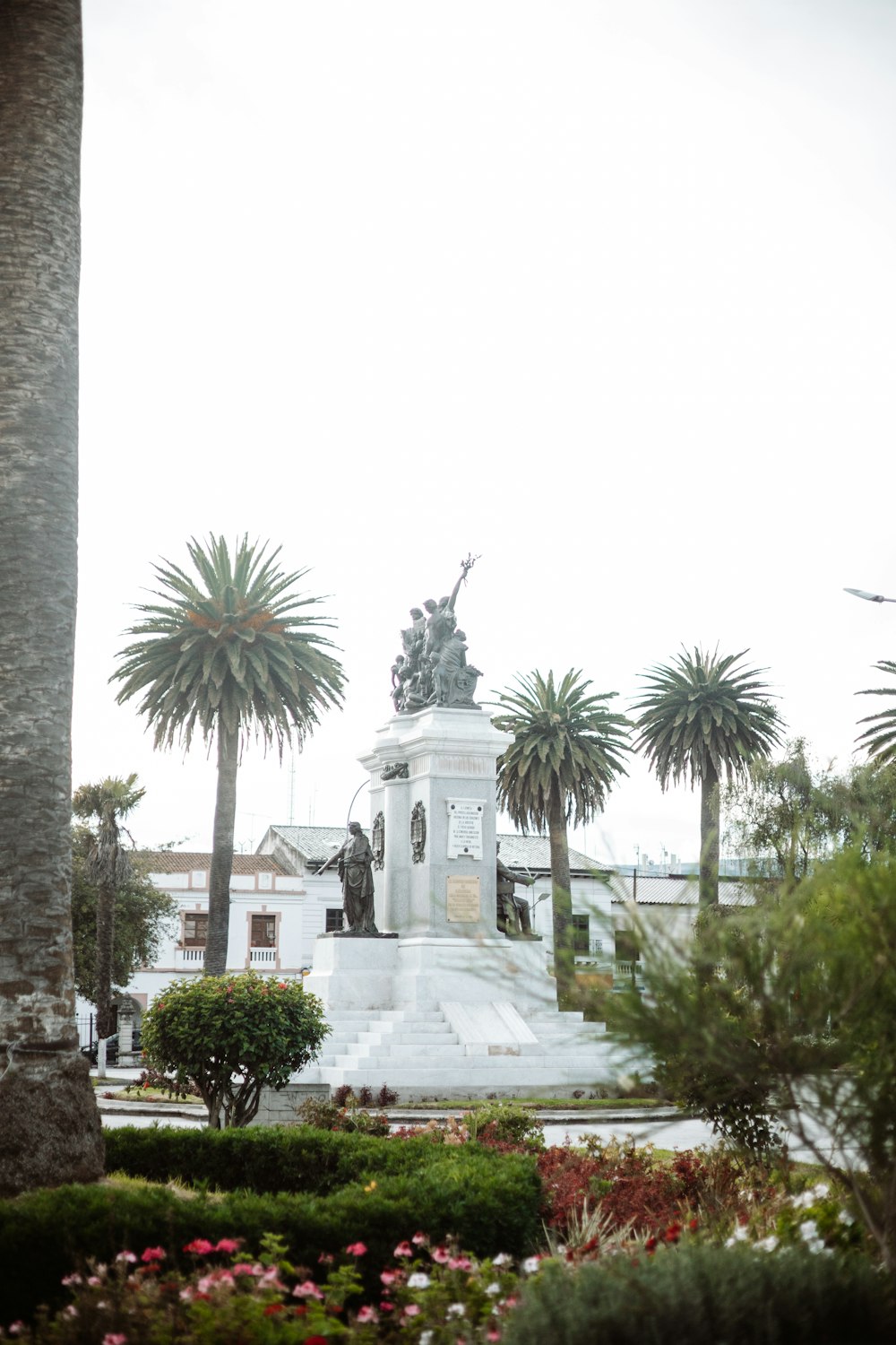 a statue in the middle of a park surrounded by palm trees
