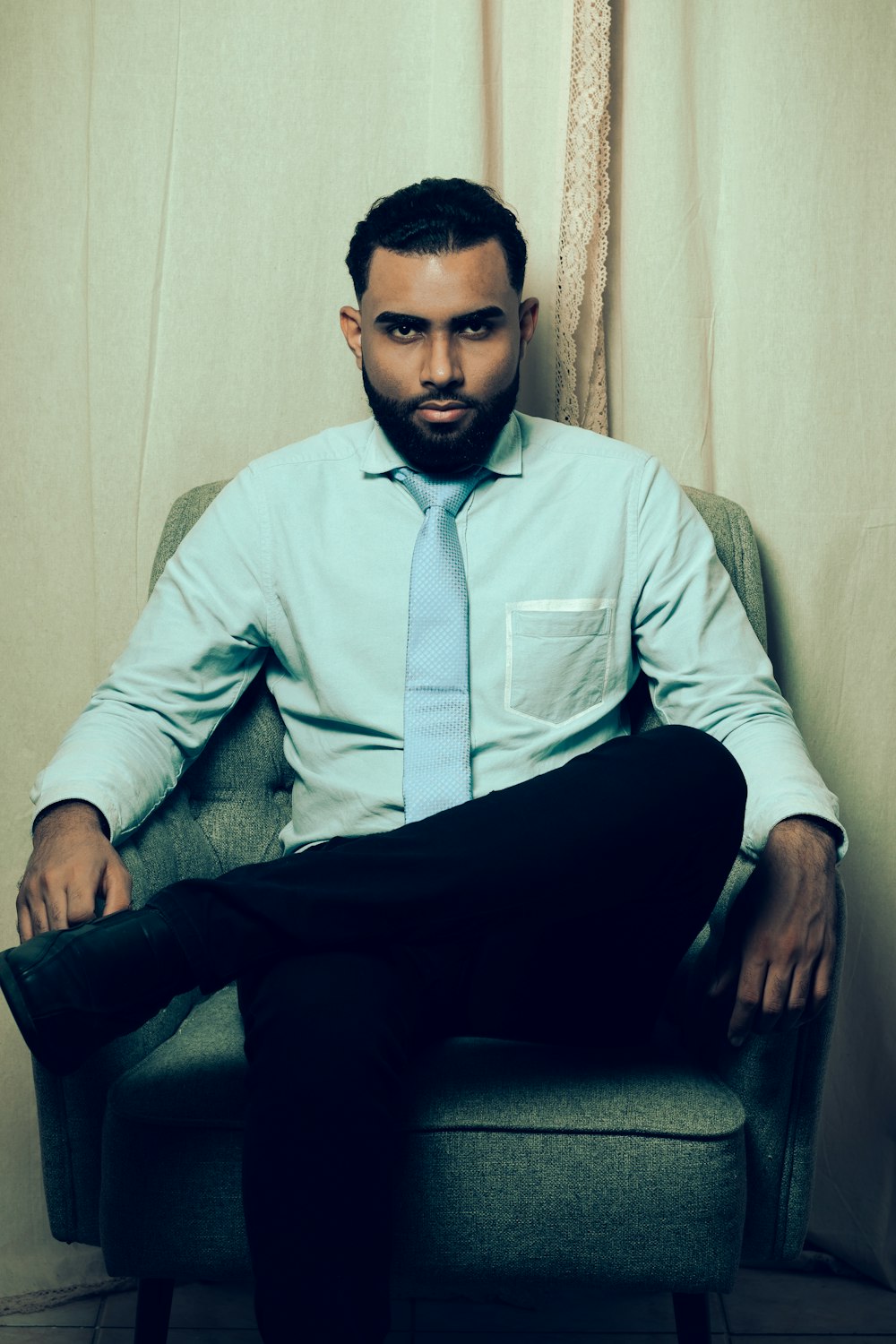 a man in a blue shirt and tie sitting on a chair