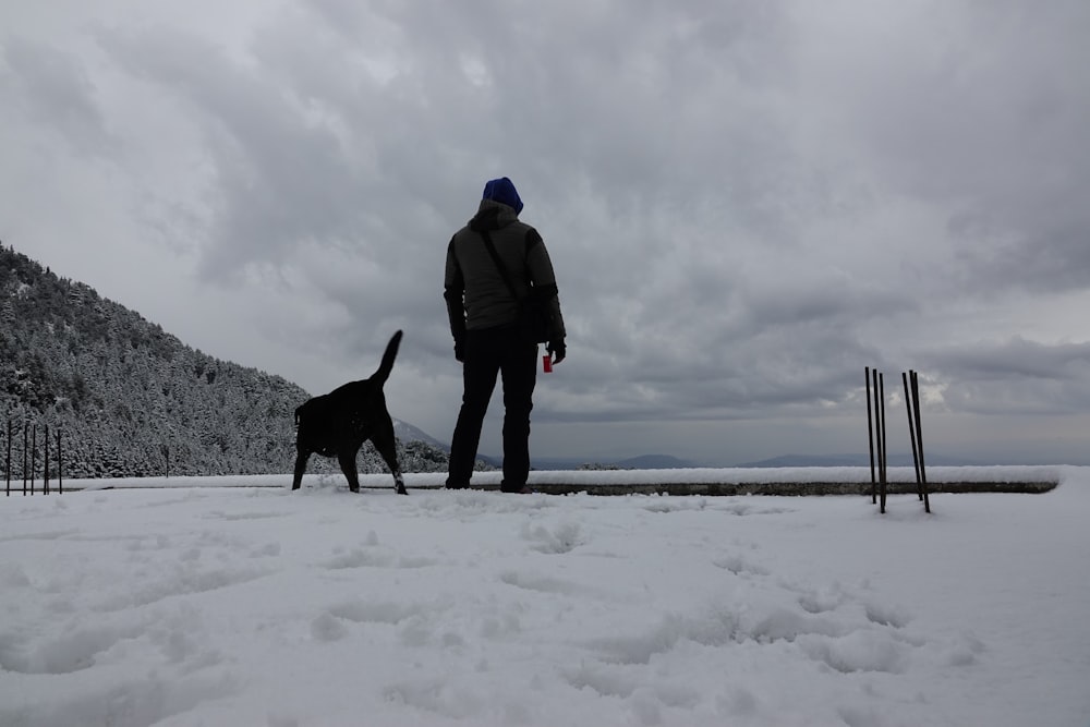 a man standing next to a dog in the snow