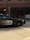 A police car from Vancouver is in motion on a city street. The car is a black and white vehicle with the word 'POLICE' and an emblem visible on the side. The background is blurred, indicating speed, and includes urban elements like an intersection and traffic lights.