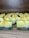 Multiple handmade soap bars are arranged in rows on a wooden surface. Each soap bar has a gradient appearance, transitioning from dark green at the bottom to yellow and white at the top. Small orange bits are sprinkled on the top of each soap bar. The brand name 'Himeriez' is embossed on each of the bars.