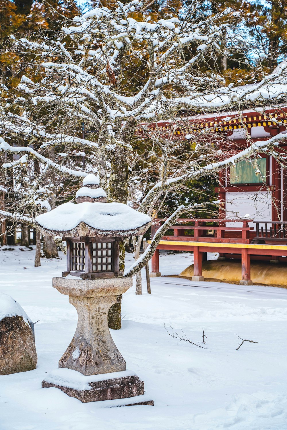 a stone lantern in the snow in front of a red building