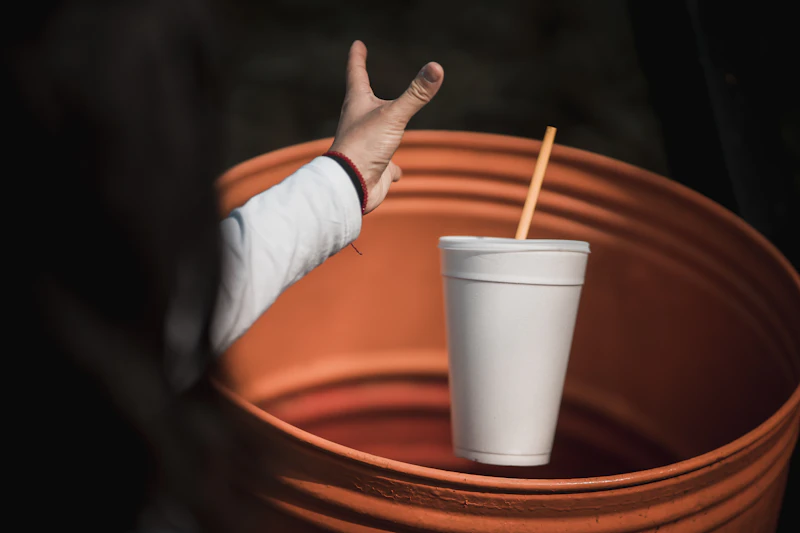 A hand reaching out to a single-use cup with a straw — illustrating the plastic packaging problem we help businesses solve.