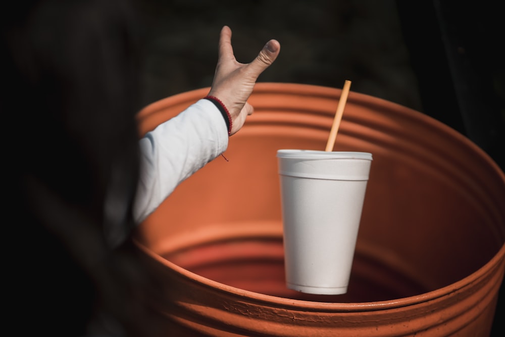 a hand reaching out to a cup with a straw sticking out of it