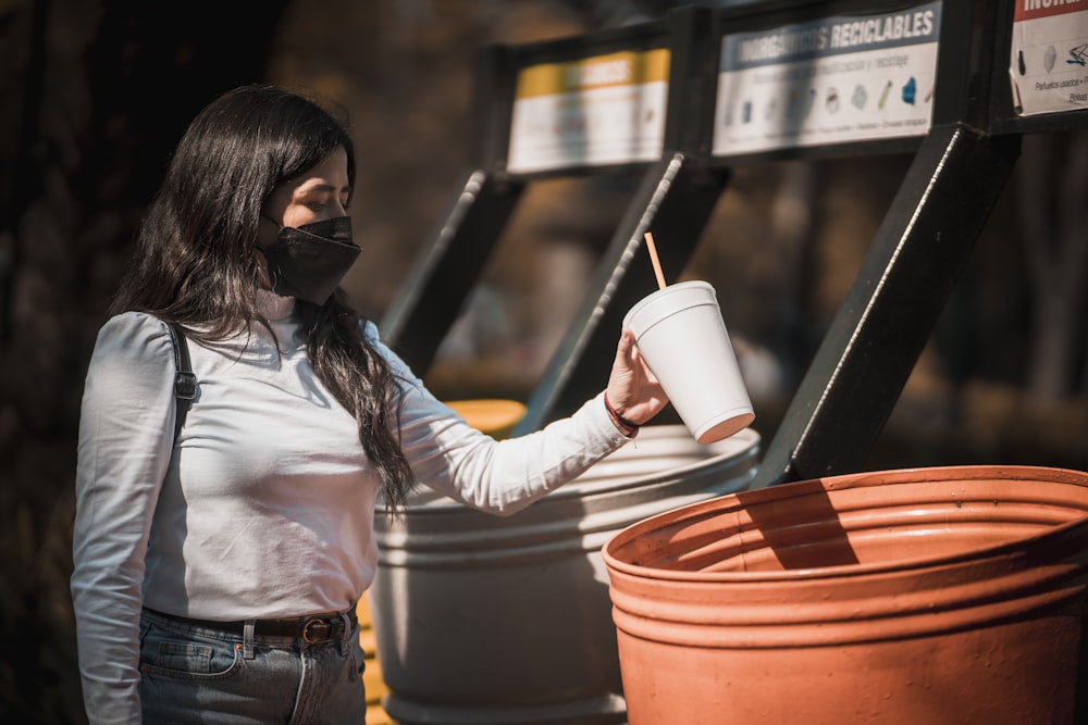 una donna che indossa una maschera facciale e tiene in mano una tazza