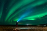 a man standing in a field watching the aurora bore