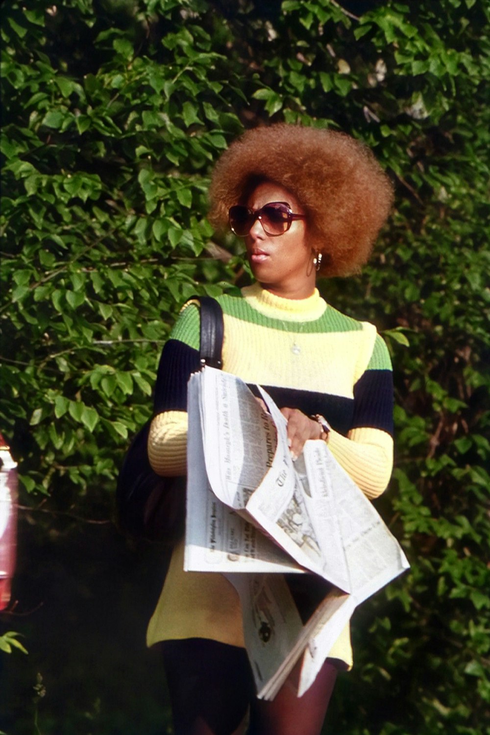 Eine Frau mit einem Afro hält eine Zeitung in der Hand