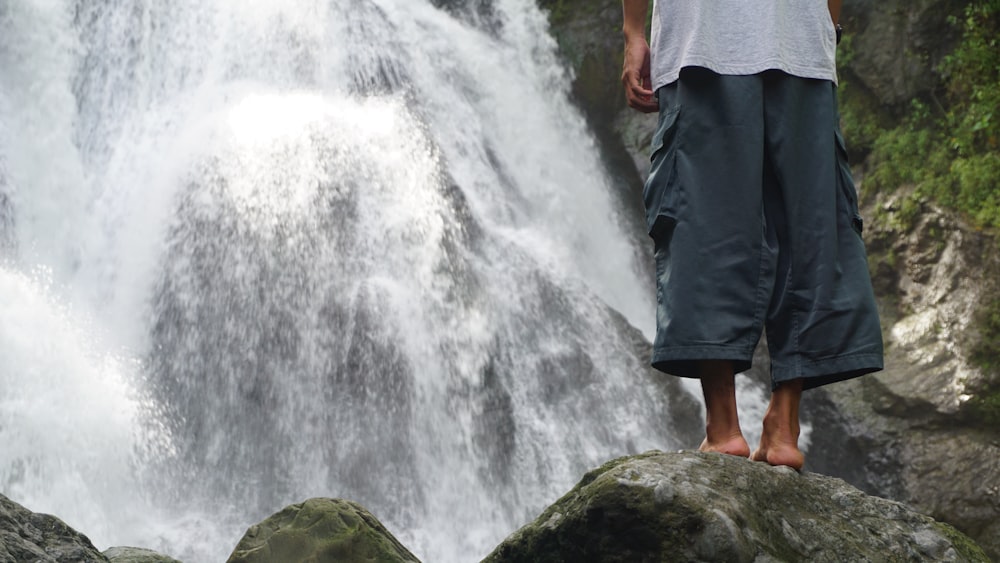 a man standing on a rock in front of a waterfall