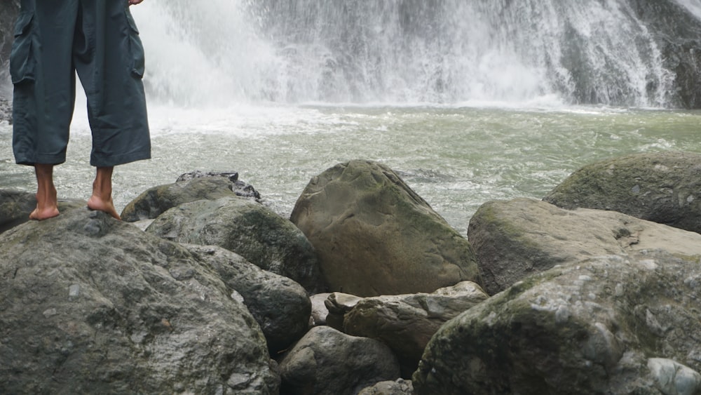 a person standing on a rock in front of a waterfall