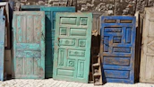 A collection of painted doors leaning against a wall, each with unique patterns and colors.