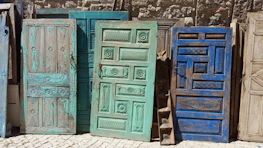 A collection of painted doors leaning against a wall, each with unique patterns and colors.