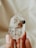 A hand is holding a clear crystal with dark inclusions inside. The background is out of focus, featuring soft, neutral colors that enhance the transparency and texture of the crystal.
