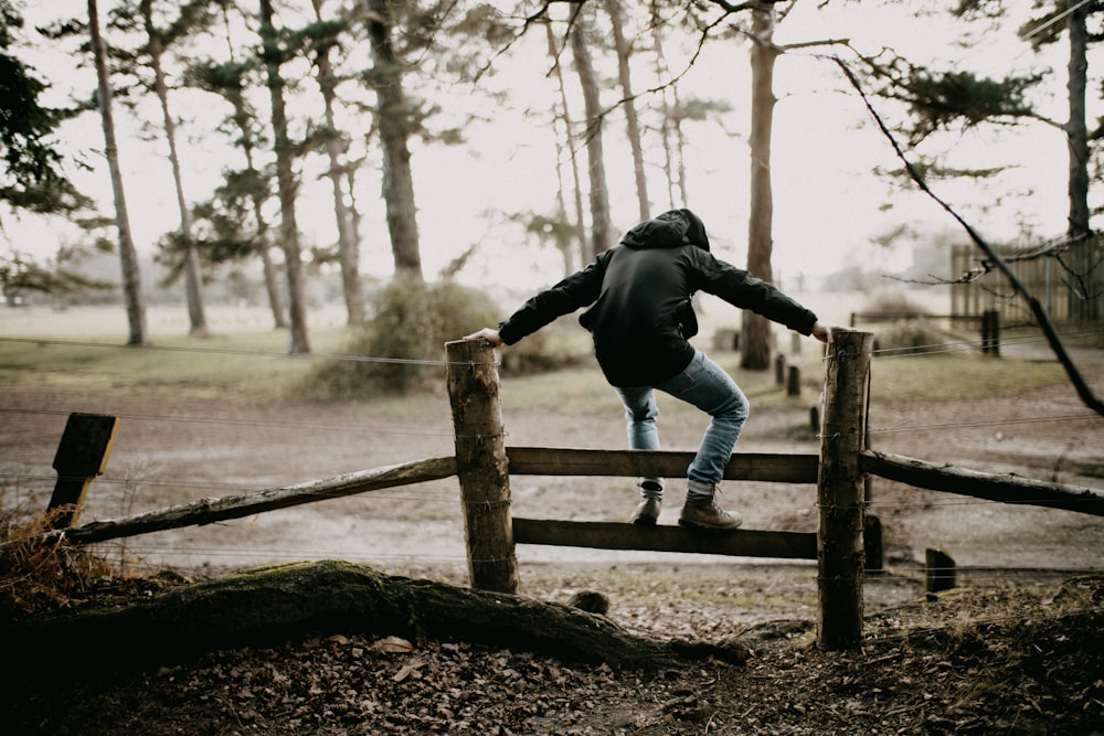 a person jumping over a wooden fence in the woods