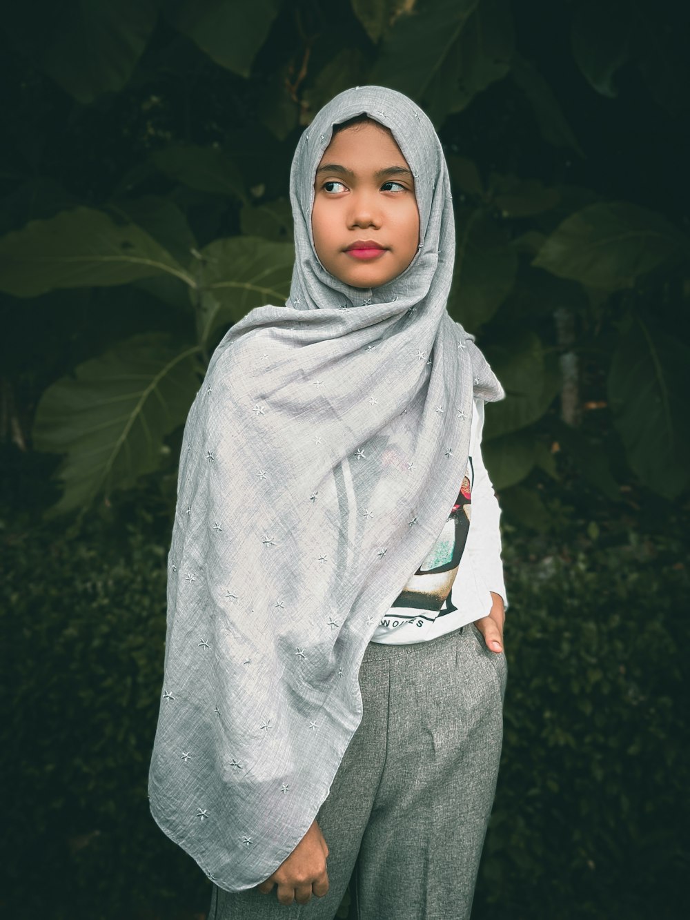 a woman wearing a white scarf standing in front of a bush