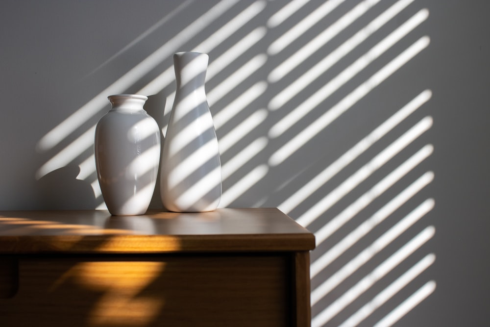 three white vases sitting on top of a wooden table