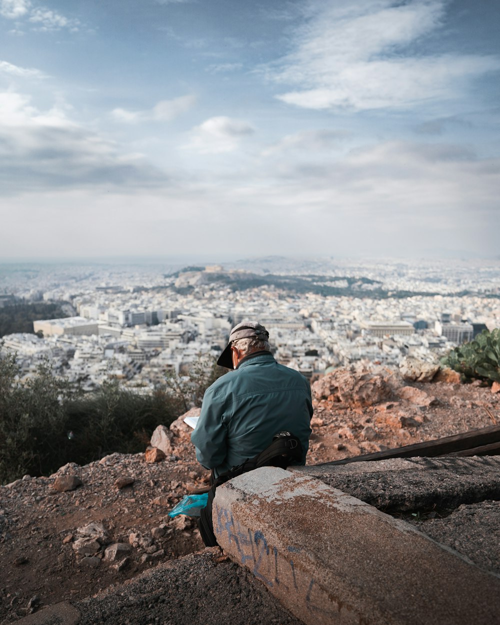 a man sitting on top of a hill talking on a cell phone