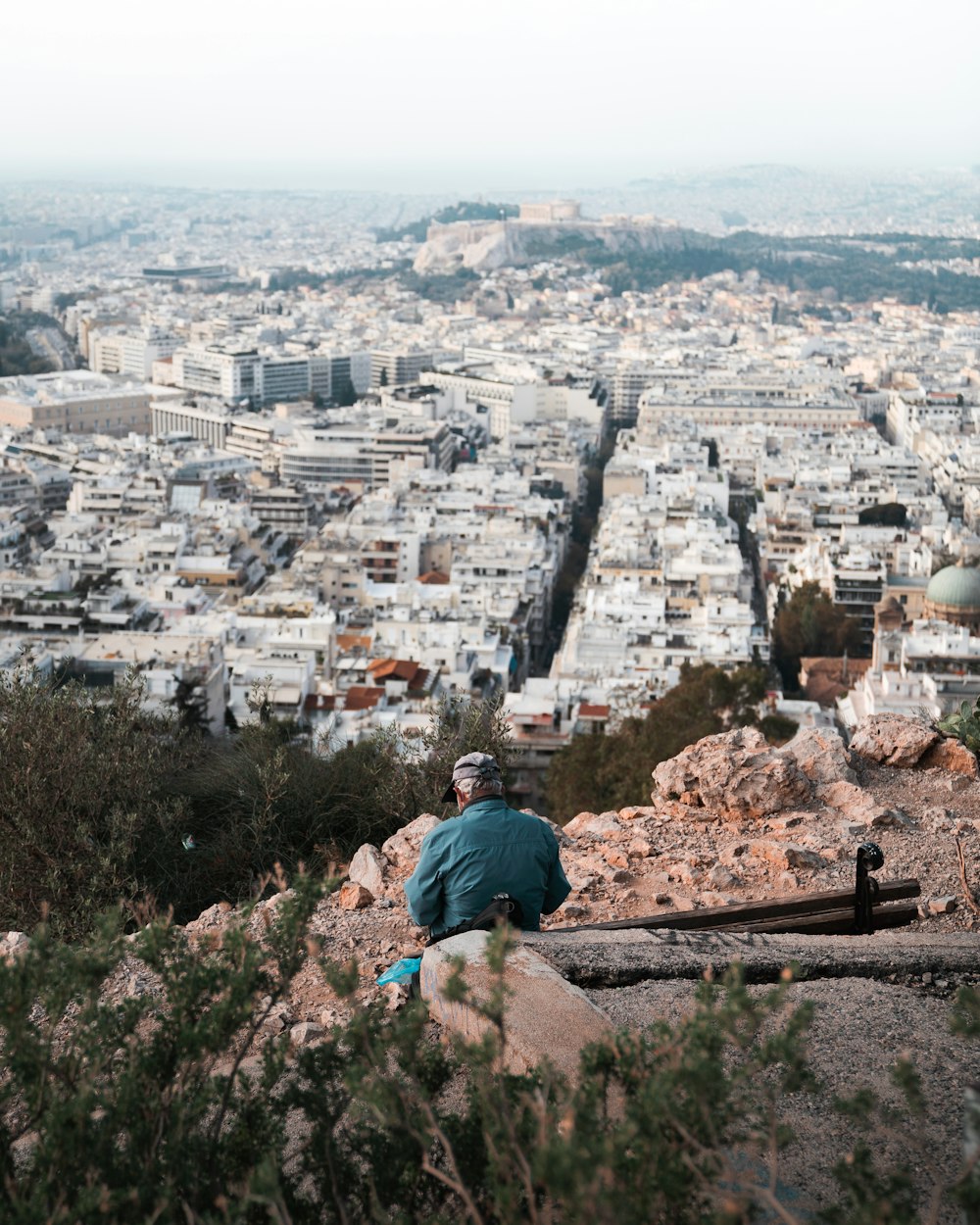 a man sitting on top of a hill overlooking a city