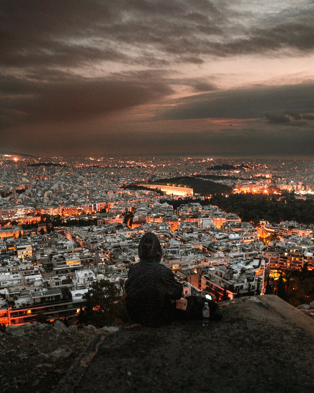 a man sitting on top of a hill overlooking a city