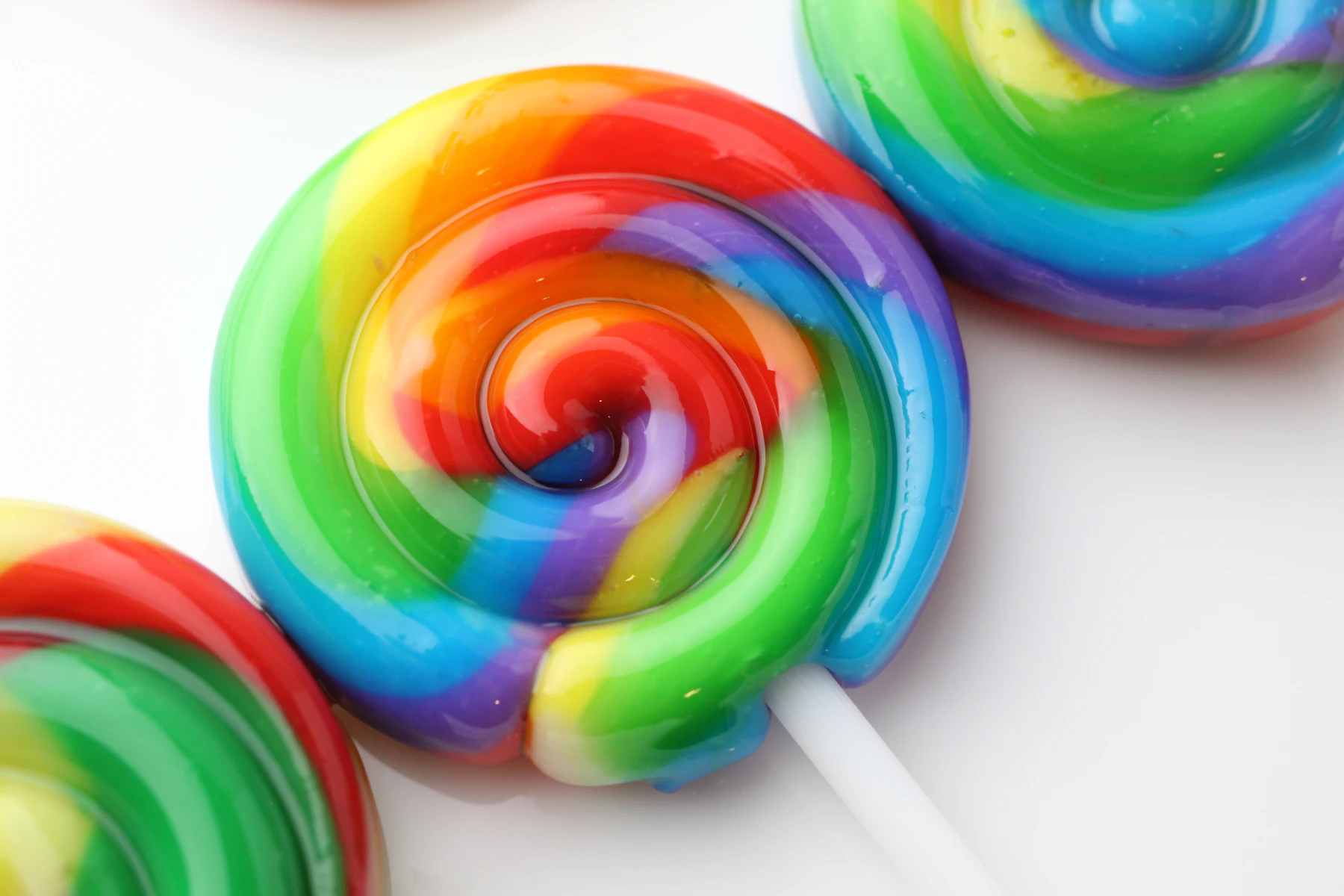 Rainbow swirl lollipops on white sticks, close up on a white surface