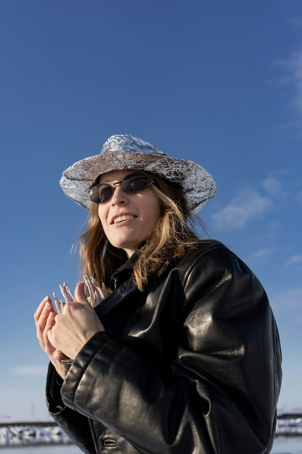 a woman wearing a hat and sunglasses standing in front of a bridge