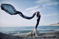 a woman standing on top of a rock near the ocean