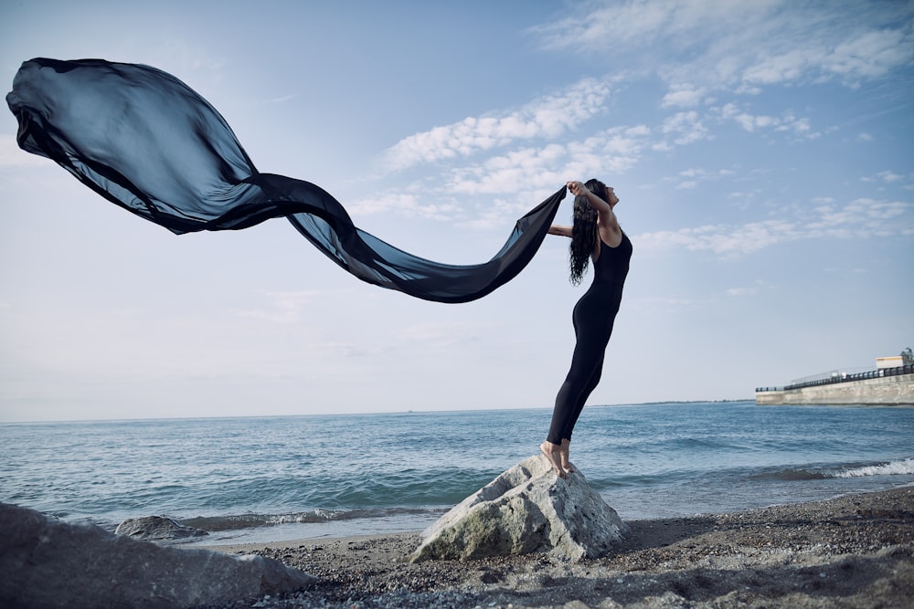 a woman standing on top of a rock near the ocean