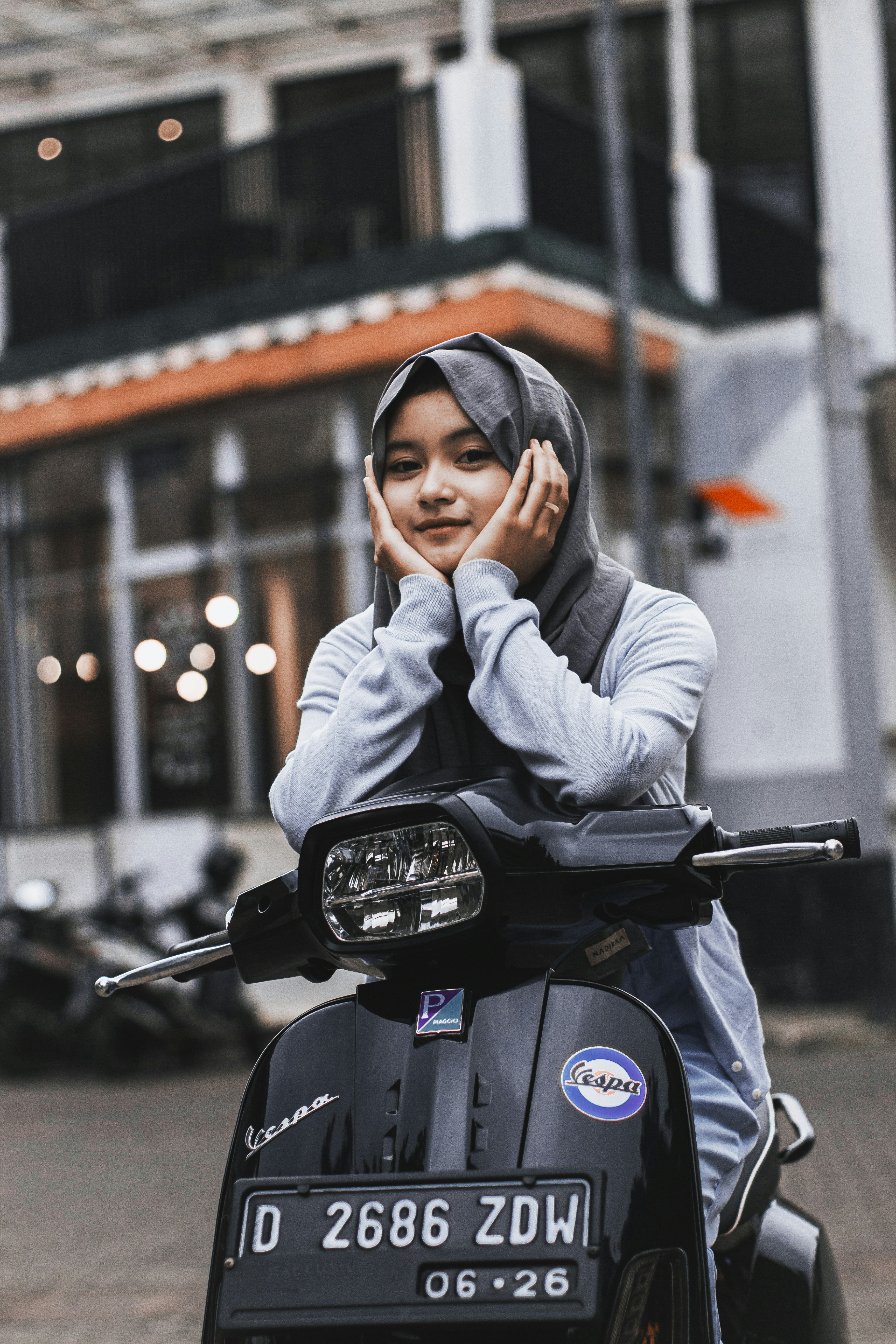 Seorang wanita mengenakan jilbab duduk di atas sepeda motor